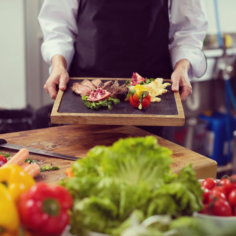 female Chef  in hotel or restaurant kitchen holding grilled beef steak plate with vegetable decoration